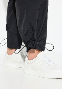 Svarta tapered byxor med dragsnöre vid anklarna, i kombination med vita perforerade sneakers med platta snören och texturerade sidor.
