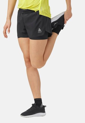 Personne en short de sport noir et haut jaune étirant la jambe en tenant le pied derrière tout en se tenant sur une jambe.