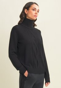 Pull noir avec un col montant côtelé, présentant des motifs en maille torsadée et des poignets et un ourlet côtelés. Texture lisse et coupe décontractée.