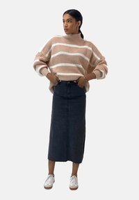 Dicker Strickpullover in Beige mit weißen Streifen, kombiniert mit einem langen schwarzen Jeansrock und weißen Sneakern. Einfaches, lässiges Design.