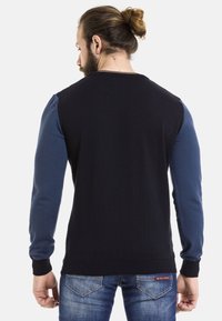 Herrenpullover mit einem dunkeln Marineblauem Körper und hellblauen Ärmeln, strukturiertem Strick, gerippten Bündchen und Saum. Die Rückansicht zeigt eine Farbblockierung.