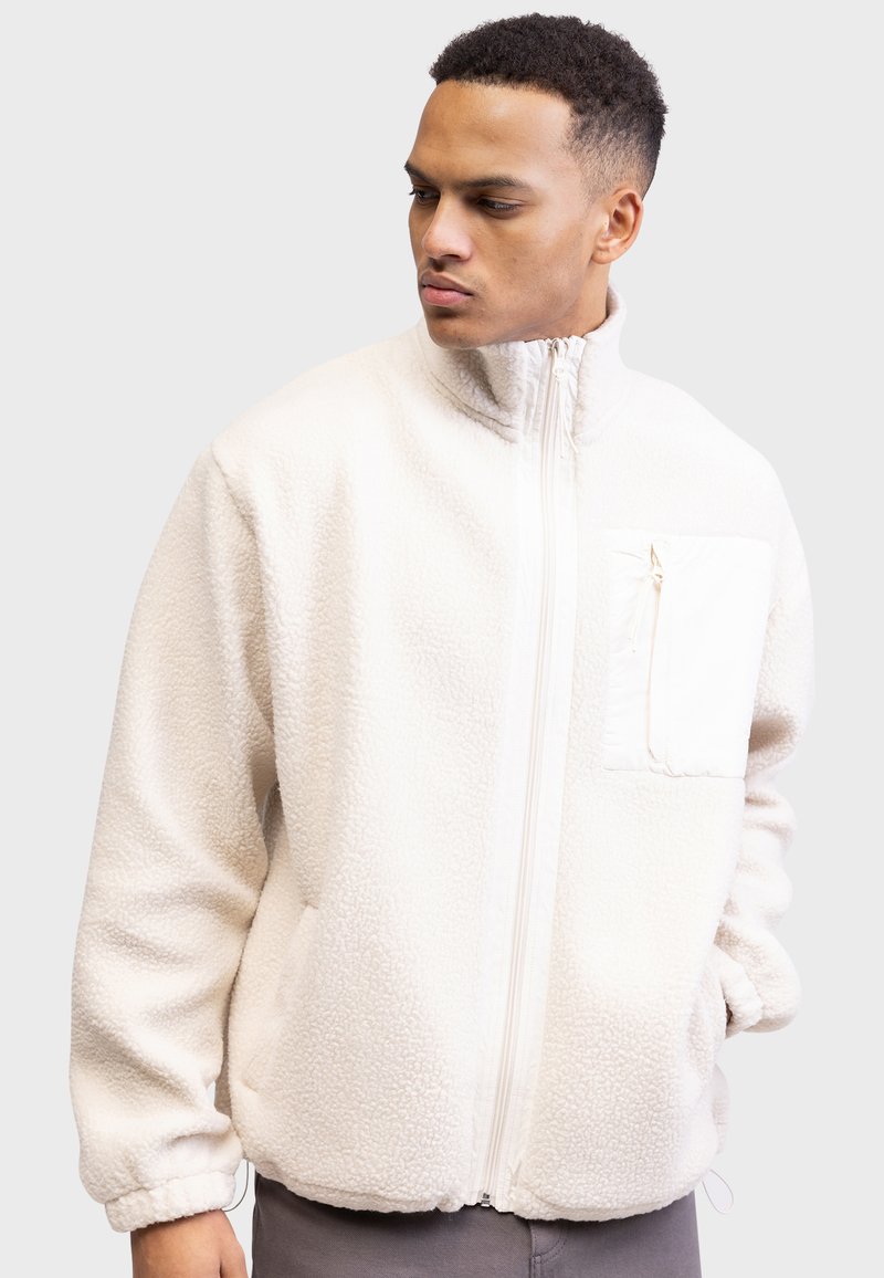 Weiße Fleecejacke mit hohem Kragen, durchgehendem Reißverschluss und Fronttasche. Verfügt über einen strukturierten Stoff und elastische Bündchen für eine enge Passform.