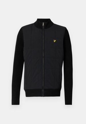 Schwarze Steppweste mit gerippten Ärmeln, Stehkragen, Frontreißverschluss und einem kleinen gelben Logo auf der Brust, mit einem gesteppten Design.