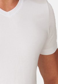 Weißes Baumwoll-T-Shirt mit kurzen Ärmeln und V-Ausschnitt. Glatte Textur mit figurbetontem Schnitt. Minimale Nähte und keine sichtbaren Muster oder Akzente.