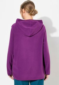 Sudadera con capucha de color púrpura, de manga larga y fabricada en un tejido suave. Presenta un bolsillo canguro y un corte holgado, con un dobladillo recto.