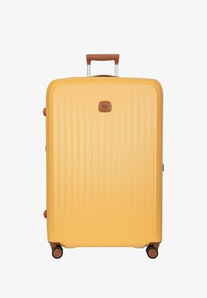 Valigia rigida gialla con scanalature verticali, manico marrone e quattro ruote nere su sfondo bianco.