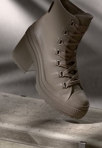 Beige leather ankle boot with a chunky heel, lace-up design, textured upper, and rubber sole featuring a patterned trim.