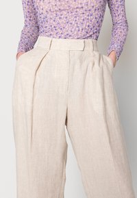 Pantalon en lin beige avec une coupe ample et jambes larges. Comprend des plis à la taille et des poches latérales. Texture lisse et légère.