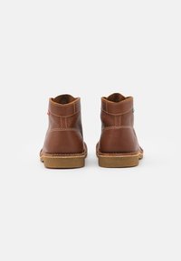 Stivaletti in pelle marrone con una superficie liscia, cuciture a contrasto e suola in gomma. Presentano un tacco basso e un design minimalista.