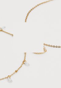 Collana in oro con cristalli trasparenti a goccia e un pendente decorativo con una fila di piccole perle. Texture liscia e lucida.