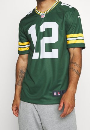 Osoba nosząca zielony i żółty jersey NFL z numerem 12, w połączeniu z jasnoszarymi szortami, pokazując tatuaże na obu przedramionach.