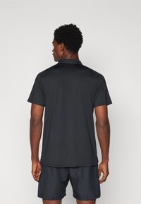 Black athletic polo shirt with short sleeves, featuring a collar and a smooth texture. Worn with matching black shorts. Back view displayed.