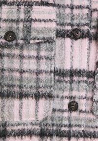 Tela de cuadro en tonos rosa y gris, con una composición de lana suave y texturizada, que presenta botones negros y un detalle de bolsillo en el pecho.