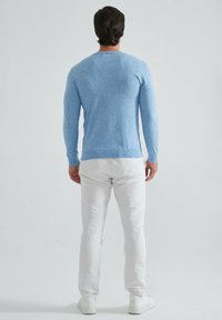 Pull en tricot bleu clair à manches longues, avec des poignets et un ourlet côtelés. Porté avec un pantalon blanc et des baskets blanches, vu de dos.