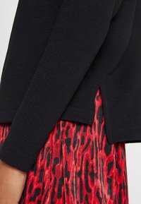 Haut noir côtelé à manches longues avec une coupe légèrement évasée et des fentes latérales, associé à une jupe rouge à imprimé léopard avec un design fluide.