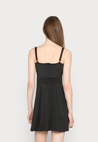 Vestido preto sem mangas com alças ajustáveis, corpete justo e saia evasé. Apresenta um fecho discreto nas costas. Textura suave.