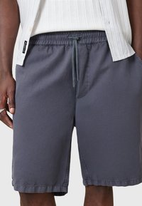 Pantaloni corti grigi realizzati in un tessuto leggero, con vita elasticizzata e cordino, tasche laterali e cuciture piatte per una finitura liscia.
