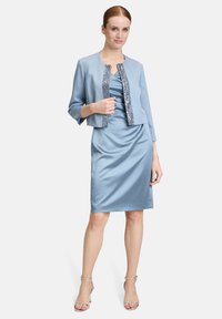 Jasnoniebieska satynowa sukienka z marszczeniami, w połączeniu z dopasowaną krótką kurtką z cekinowym wykończeniem i rękawami o długości trzech czwarte.