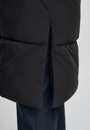 Giubbotto imbottito nero con zip visibile, sezione inferiore ventilata e superficie liscia e opaca. Realizzato con una silhouette elegante.