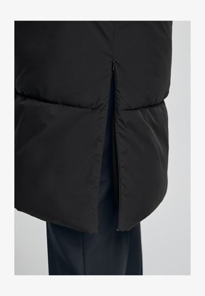 Zwarte gewatteerde jas met een zichtbare rits, een geventileerd onderste gedeelte en een gladde, matte textuur. Gestyled met een slanke silhoeet.