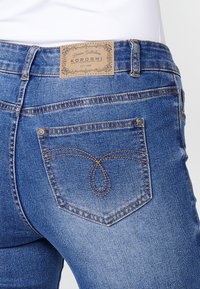 Blå denimjeans med midjehög midja, distinkta sömmar på bakfickorna och en läderlogotyp på midjebandet.