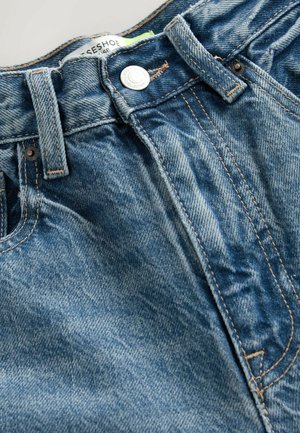 Denim jeans feature a light blue color with whiskering details. The waistband includes a metal button and visible stitching along seams.
