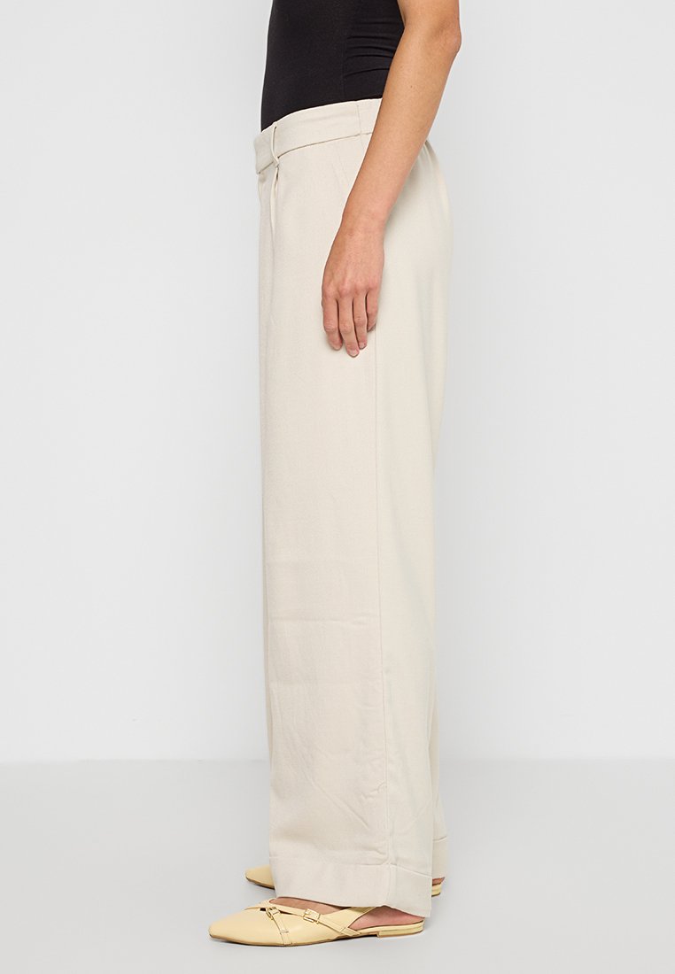 Beige weite Hosen aus leichtem Stoff, mit maßgeschneidertem Bund und einer glatten, fließenden Textur. Einfaches Design ohne sichtbare Muster.