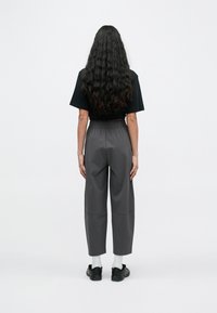 Szürke, laza szabású nadrág rugalmas derékpánttal, fekete, rövidített pólóval párosítva. Az anyag simának tűnik, finom textúrával.