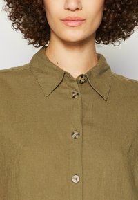 Olivgrön skjorta med knappar och krage, som har klassiska knappar och ett texturerat tyg för en naturlig look.