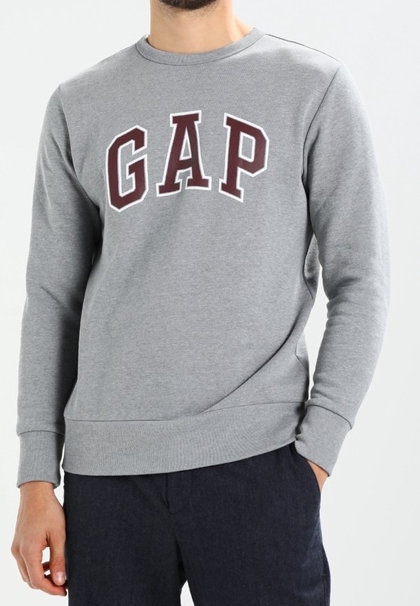 Harmaa collegepaita, joka on valmistettu puuvillasekoitteesta, jossa on ribbaus kauluksessa ja pitkät hihat. "GAP" -logo burgundin värisessä sävyssä edessä.