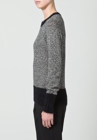 Pull en maille mélangée gris et noir, avec un corps texturé, des poignets côtelés noirs et un large ourlet côtelé noir.