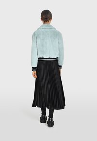 Giacca in pelliccia sintetica azzurro chiaro con ampio colletto, abbinata a una gonna plissettata nera e stivaletti neri. Polsini e fascia in vita a righe.