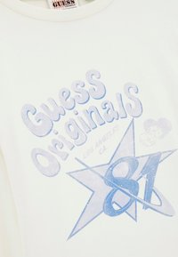 Witte katoen t-shirt met blauwe grafische tekst: "Guess Originals Los Angeles CA" en een ster met ontwerp "81", textuurdruk.