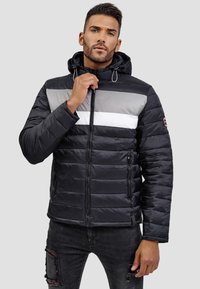 Chaqueta acolchada negra con una franja horizontal gris y blanca en el pecho. Cuenta con capucha, cierre frontal con cremallera y bolsillos laterales.