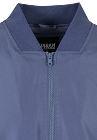 Gros plan d'une veste bleue zippée avec un col côtelé et une étiquette de la marque Urban Classics visible à l'intérieur.
