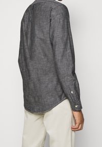Camisa de manga larga en tejido gris oscuro, con un cuello clásico, puños abotonados y un dobladillo curvado, con un acabado texturizado.