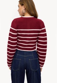 Suéter de punto a rayas rojas y rosas con mangas largas, con cuello redondo y tejido texturizado, combinado con pantalones vaqueros de cintura alta.