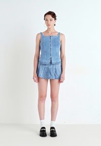 Lichtblauwe denimoutfit met een aansluitend tanktop met knopen en een uitlopende minirok. Inclusief witte sokken en zwarte gesloten schoenen.
