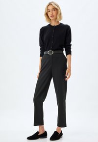 Cardigan nero con bottoni, abbinato a pantaloni neri a vita alta e scarpe slip-on nere. Tessuto morbido e vestibilità su misura.