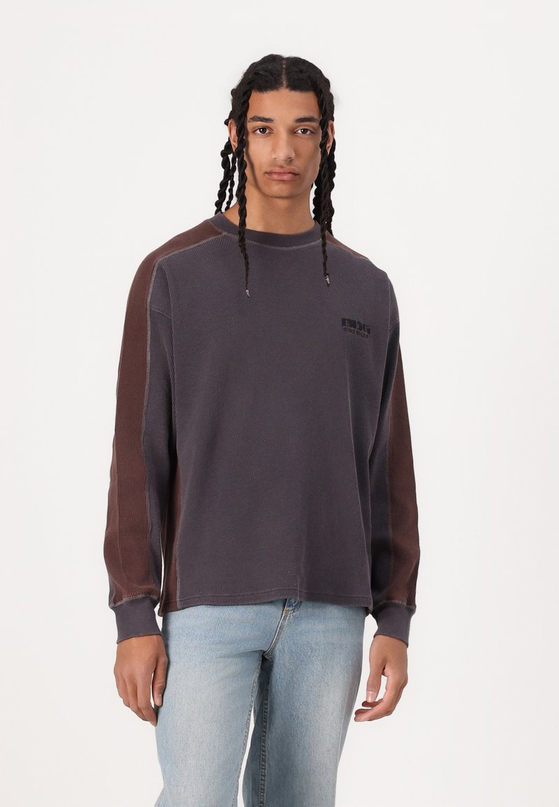 Langærmet skjorte i mørkegrå med brune accenter, ribbet tekstur, afslappet pasform og logodetalje på forsiden. Båret med lyseblå jeans.