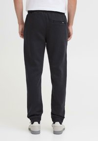 Czarne spodnie dresowe wykonane z miękkiego materiału, wyposażone w elastyczną talię, prążkowane mankiety oraz małą tylną kieszeń. Noszone z białymi butami.