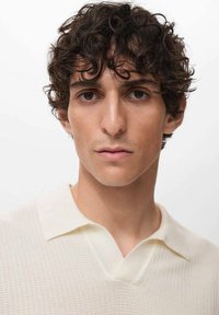 Knit polo sweater in off-white, featuring a V-neck and collar, with a textured pattern and ribbed detailing at the hem sleeves.