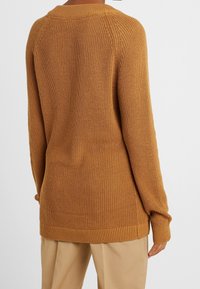 Senfgelber, gestrickter Pullover mit strukturiertem Gewebe, gerippten Bündchen und einem leicht verlängerten Saum hinten für zusätzlichen Komfort.