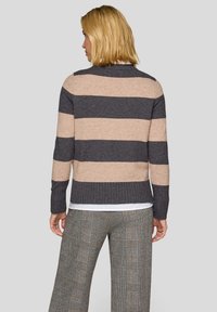 Gestrickter Pullover mit breiten horizontalen Streifen in Beige und Dunkelgrau, mit geripptem Saum und Bündchen. Kombiniert mit karierten, hochtaillierten Hosen.