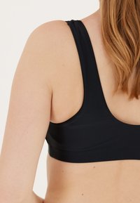 Musta urheiluhaalari, jossa on leveät hihnat, sileä pinta ja racerback-muotoilu, joka esittelee matalan leikkauksen selässä ja vähäiset ompelutiedot.