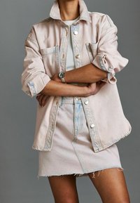 Veste en denim rose clair avec deux poches avant et boutons argentés, associée à une mini-jupe assortie en rose clair avec des bords effilochés.