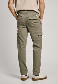 Pantalones cargo verde oliva hechos de tejido duradero, con múltiples bolsillos y un diseño de pierna ajustada. Llevados con zapatillas blancas.
