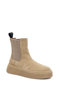 Botín de ante beige hasta el tobillo con paneles elásticos en los laterales, suela acanalada y un tirador en el talón. Elementos texturizados añaden interés visual.