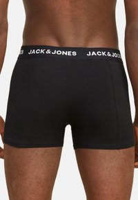 Caleçons boxeurs noirs en stretch avec une coupe ajustée, dotés d'une ceinture élastique douce imprimée avec "JACK & JONES" en blanc. Texture de tissu lisse.