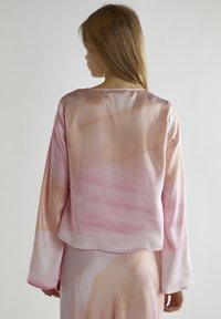 Seidenbluse in zartem Rosa mit abstrakten Aquarellmustern, mit langen Ärmeln und einem entspannten Ausschnitt. Glatte und glänzende Textur.